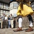 Eine Person in historischer Kleidung mit Schwert steht vor einer Gruppe vor Fachwerkhäusern.