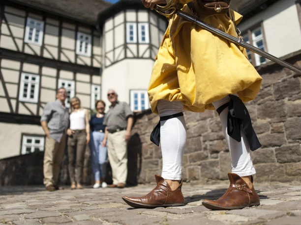 hx_fuehrung_jostziegenhirt_andreashub.jpg Eine Person in historischer Kleidung mit Schwert steht vor einer Gruppe vor Fachwerkhäusern.