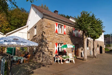 Historische Mühle Nespen Historisches Steinhaus mit rot-weißen Fensterläden, Gäste genießen Sonne an Tischen im Freien.