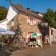 Historische Mühle Nespen Historisches Steinhaus mit rot-weißen Fensterläden, Gäste genießen Sonne an Tischen im Freien.