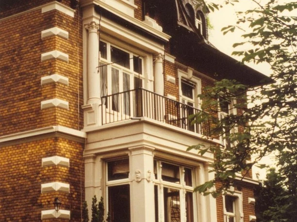 Villa Reusch Gründerzeitliche Villa mit Erker und kunstvollen Verzierungen, umgeben von Bäumen und Sträuchern.