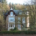 Villa Karl Reusch Charmante Villa mit weißem Dekor, umgeben von herbstlichen Bäumen und üppigem Grün, vor Waldkulisse.