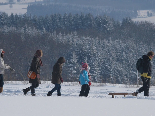 Winterwandern Eine Familie wandert im Schnee durch eine winterliche, bewaldete Landschaft, ein Schlitten wird gezogen.