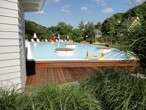 Kinderbecken Ein Außenpool mit Liegestühlen, umgeben von üppiger Natur bei sonnigem Wetter.
