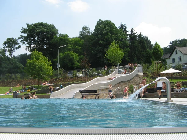 Schwimmerbecken Menschen genießen ein Schwimmbad mit einer weißen Rutsche im Freien, umgeben von grünen Bäumen.