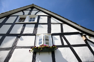 Fachwerkhäuser im Ortsteil Bruch Fachwerkfassade eines Hauses mit blühenden Blumenkästen unter einem Himmel mit wenigen Wolken.