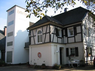 Kornbrennerei Müllenbach Fachwerkhaus mit weißen Wänden, Schindeldach und separatem Turm, umgeben von Herbstlaub.