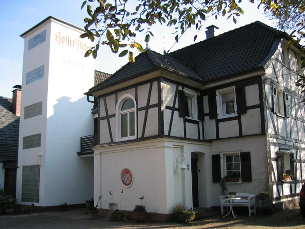 Kornbrennerei Müllenbach Fachwerkhaus mit weißen Wänden, Schindeldach und separatem Turm, umgeben von Herbstlaub.