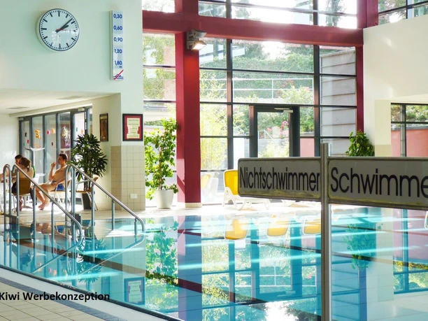 Schwimmbecken Innenansicht eines Schwimmbades mit Uhr an der Wand, Schwimmbecken und Sitzbereich.