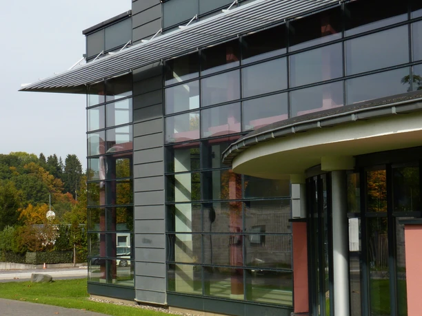 Außenansicht Modernes Gebäude mit gebogener Glasfassade und markantem Dekor, umgeben von Grünflächen.