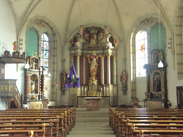 Pfarrkirche, Innenansicht Kircheninnenraum mit prächtigem Altar, bunten Glasfenstern und geschnitzten Figuren auf Podesten.