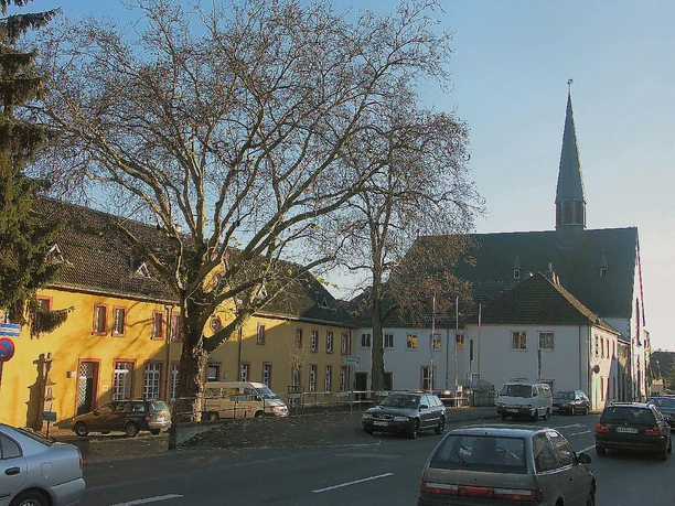 Pfarrkirche und ehem. Kloster, Vorderansicht Eine mittelalterliche Kirche mit einem markanten Turm, umgeben von historischen Gebäuden und Bäumen.