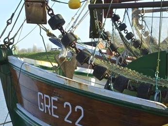 Hafen Greetsiel Kutternetz Detailansicht eines grünen Kutters mit aufgehängtem Fischernetz und schwarzen Schwimmkörpern im Hafen.
