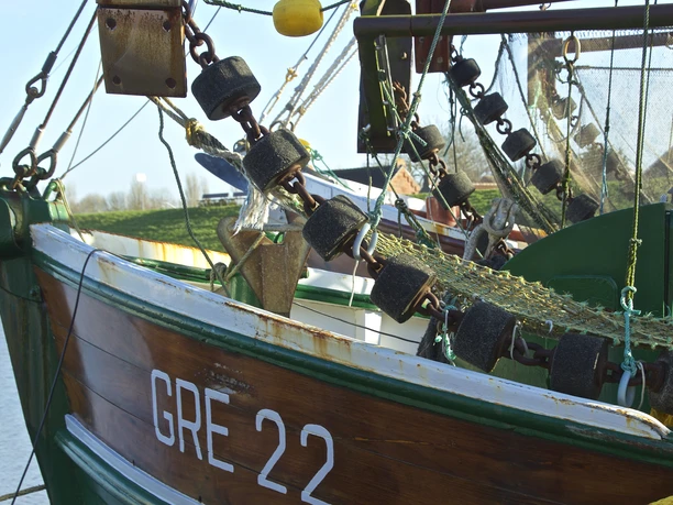 Hafen Greetsiel Kutternetz Detailansicht eines grünen Kutters mit aufgehängtem Fischernetz und schwarzen Schwimmkörpern im Hafen.