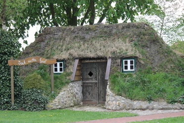 Historischer Dorfplatz Traditionelles Heuerhaus mit grasbewachsenem Dach und Holztür in einem historischen Museumsdorf