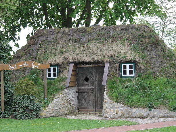 Historischer Dorfplatz Traditionelles Heuerhaus mit grasbewachsenem Dach und Holztür in einem historischen Museumsdorf