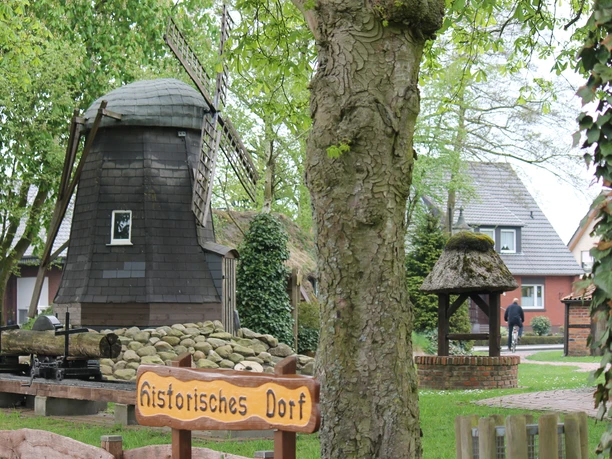 Historischer Dorfplatz Alter Dorfplatz mit kleiner Windmühle, Ziehbrunnen und Bäumen inmitten eines historischen Ensembles.