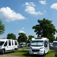 Wohnmobilstellpatz Steinhude Wohnmobilstellplatz mit mehreren Wohnmobilen unter blauem Himmel und grünen Bäumen an einem sonnigen Tag.