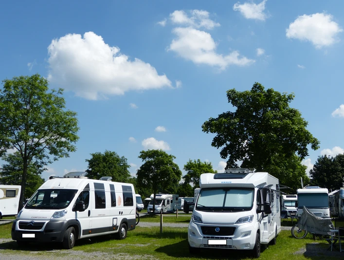 Wohnmobilstellpatz Steinhude Wohnmobilstellplatz mit mehreren Wohnmobilen unter blauem Himmel und grünen Bäumen an einem sonnigen Tag.