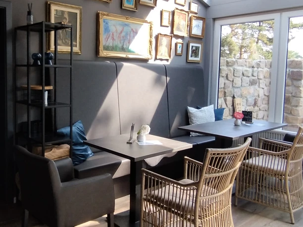 A bright café area with modern seating nooks, rattan and leather armchairs, and gold-framed wall art.