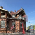 Tourist-Information Rhauderfehn im Fehn- und Schiffahrtsmuseum Westrhauderfehn Backsteingebäude mit Erker und Treppe vor blauem Himmel, davor Fahnen und Schild mit der Aufschrift 'MUSEUM' und 'TOURIST-INFO'