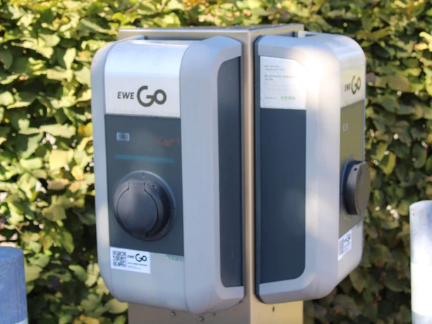 ewe-go-ladestation-oldenburger-straße2.jpg Ansicht zweier kompakter EWE Go Ladestationen vor einer grünen Hecke.