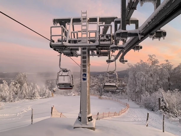 Snow-covered chairlift in a wintry landscape, evening sky in the background.