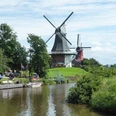 ostfrieslandrundfahrt Zwei historische Windmühlen an einem Kanal, umgeben von grüner Landschaft und blauem Himmel.