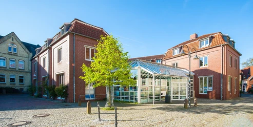 Stadtbibliothek Backsteingebäude mit Glasvorbau und rotem Dach im Sonnenschein auf gepflastertem Platz.