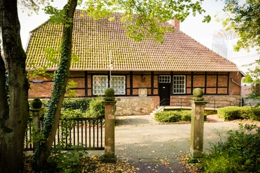 Kutscherhaus Historisches Fachwerkhaus mit rotem Ziegeldach, umgeben von Bäumen und einer kleinen Gartenanlage.