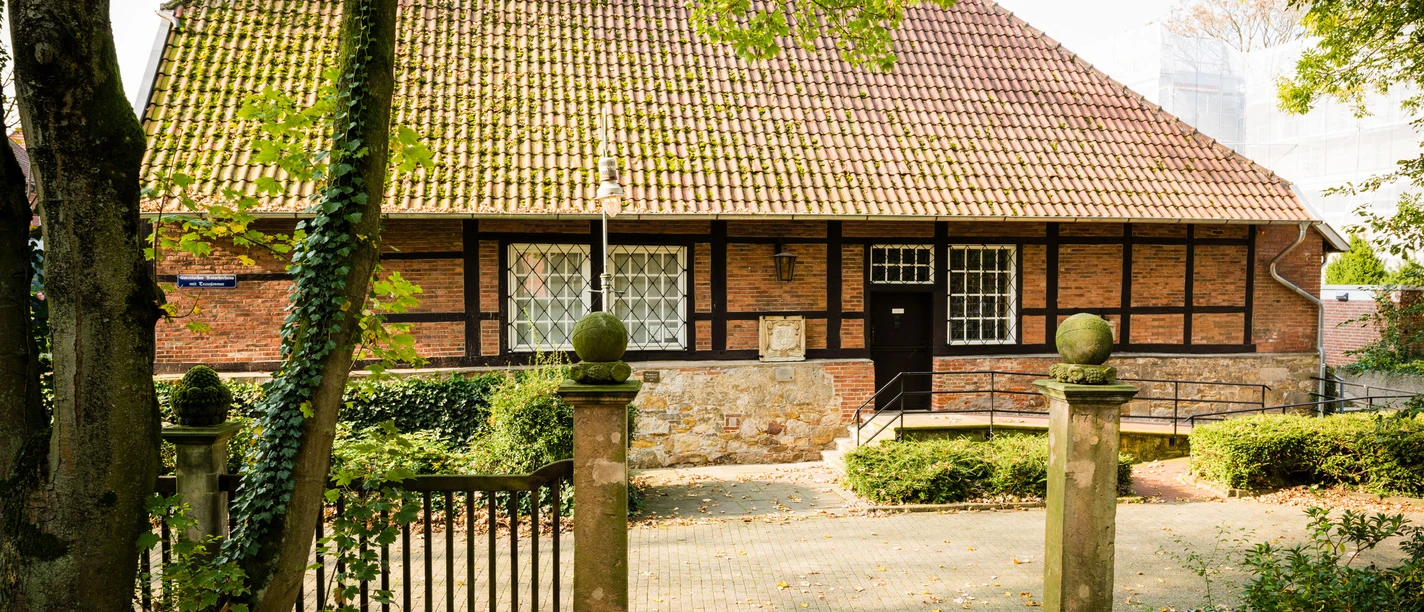 Kutscherhaus Historisches Fachwerkhaus mit rotem Ziegeldach, umgeben von Bäumen und einer kleinen Gartenanlage.