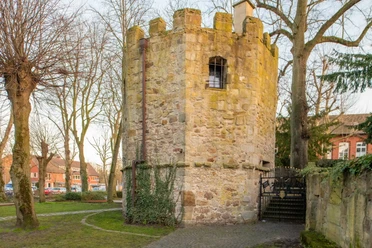 Pulverturm Runder mittelalterlicher Turm aus Naturstein mit Zinnen und kleinem Fenster, umgeben von Bäumen.