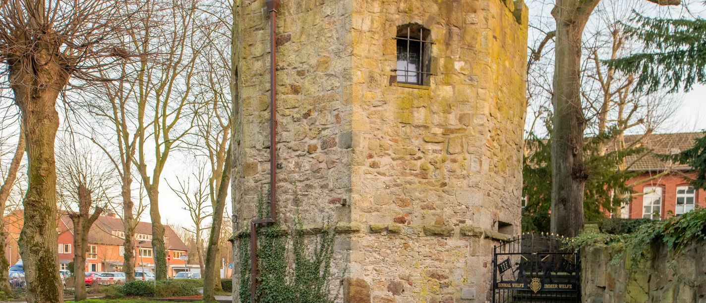 Pulverturm Runder mittelalterlicher Turm aus Naturstein mit Zinnen und kleinem Fenster, umgeben von Bäumen.