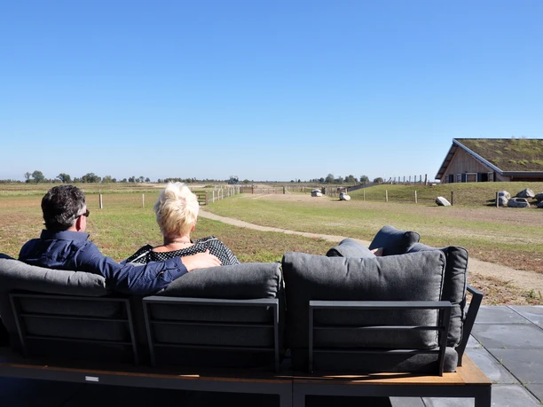 Schafstall Bargerveen Zwei Personen sitzen auf einer Bank und blicken über eine weite Moorlandschaft mit Schafstall.