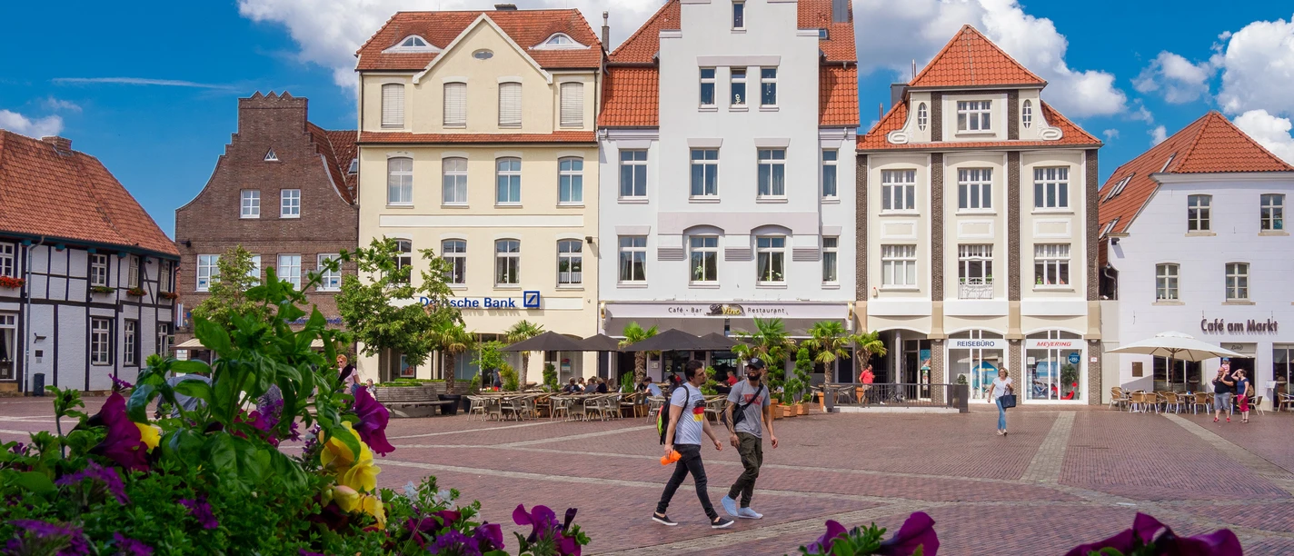 Marktplatz mit alten Bürgerhäusern Historischer Marktplatz in Lingen mit bunten Bürgerhäusern, Straßencafé und blühenden Pflanzen.