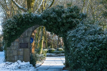Garten der Justiz Amtsgerichtpark Steinerner Torbogen mit Efeu bewachsen, führt in einen verschneiten Park mit alten Bäumen.