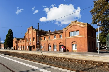 Bahnhof Lingen Historisches Backsteingebäude des Bahnhofs Lingen mit Bahnsteig und Gleisen unter blauem Himmel.