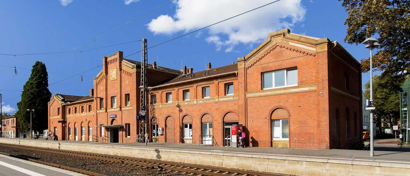 Bahnhof Lingen Historisches Backsteingebäude des Bahnhofs Lingen mit Bahnsteig und Gleisen unter blauem Himmel.