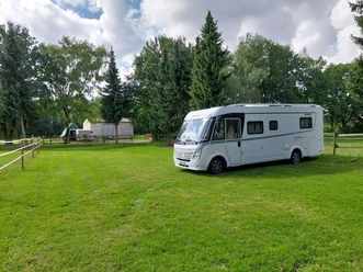 Wohnmobilstellplatz mit einem Wohnmobil auf grünem Rasen, umgeben von Bäumen und Pferdekoppel.