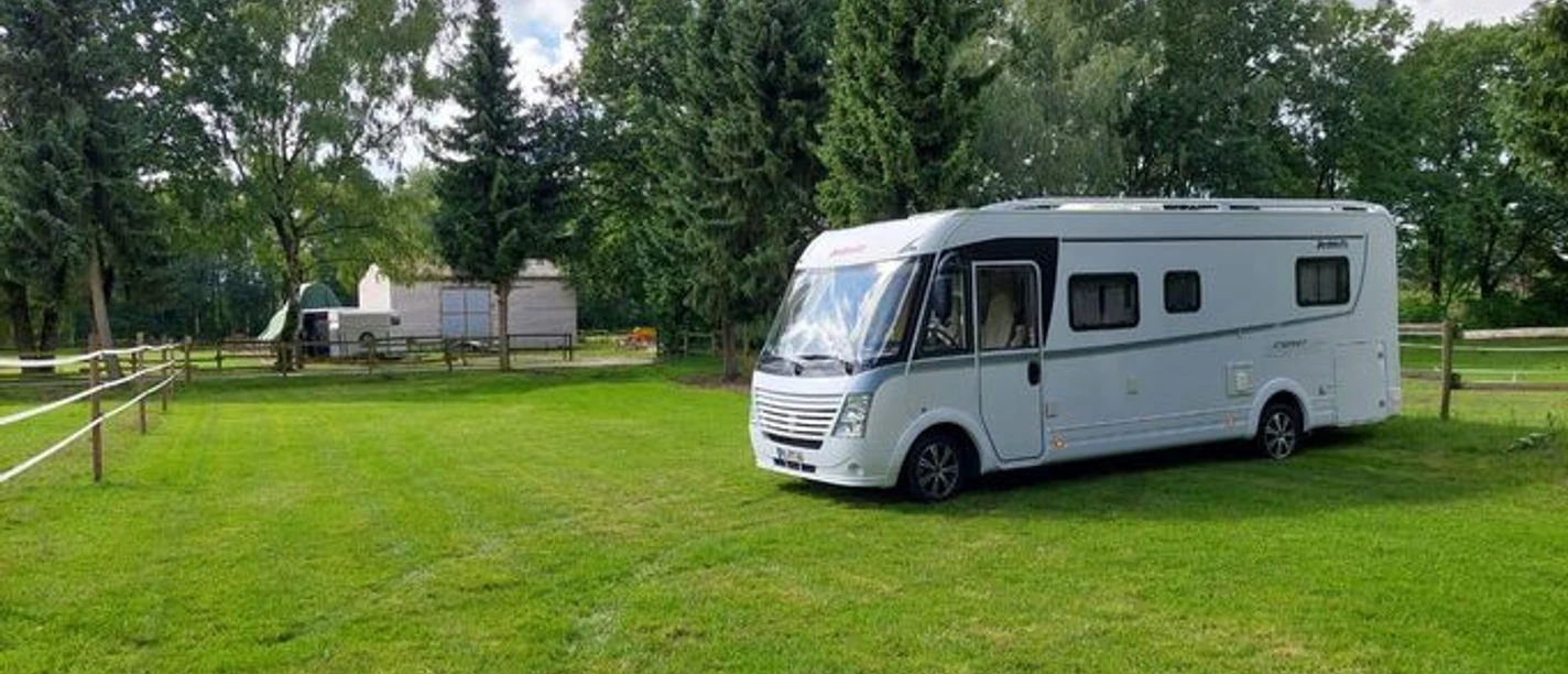 Wohnmobilstellplatz mit einem Wohnmobil auf grünem Rasen, umgeben von Bäumen und Pferdekoppel.