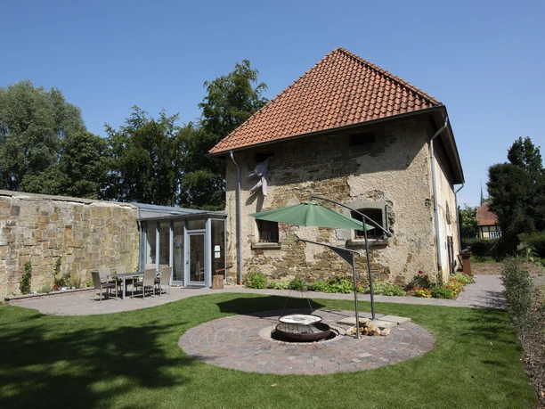 amtsgefangnis-SGFuerstenau-Osnabruecker-Land-Ausflug-Erlebnis-Uebernachtung Historischer, steinerner Gebäudekomplex mit rotem Dach, umgeben von grünem Garten.