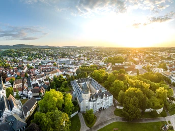 Panoramablick auf Detmold bei Sonnenuntergang, historische Gebäude von Bäumen umgeben, weite Aussicht.