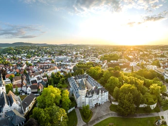 Panoramablick auf Detmold bei Sonnenuntergang, historische Gebäude von Bäumen umgeben, weite Aussicht.
