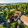 Detmold-2023-023-LWL Freilichtmuseum-Teutoburger-Wald-Tourismus-D-Ketz-CC-BY-SA.jpg Luftaufnahme zeigt ein Freilichtmuseum in Detmold mit Fachwerkhäusern und grüner, hügeliger Landschaft.