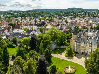 Detmold-2023-163-Residenzschloss-Schlosspark-Teutoburger-Wald-Tourismus-D-Ketz-CC-BY-SA.jpg Luftaufnahme von Detmold, zeigt das historische Residenzschloss umgeben von üppigem Grün und Stadtansicht.