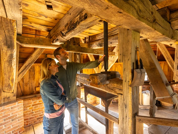 Detmold-2023-074-LWL Freilichtmuseum-Teutoburger-Wald-Tourismus-D-Ketz.jpg Ein Paar steht in einer historischen Mühle, untersucht fachwerkartige Holzkonstruktionen und Getriebe.