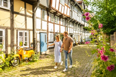 Detmold-2023-211-Adolfstraße-Teutoburger-Wald-Tourismus-D-Ketz.jpg Ein Paar spaziert bei Sonnenschein durch eine idyllische Fachwerkgasse in Detmold.