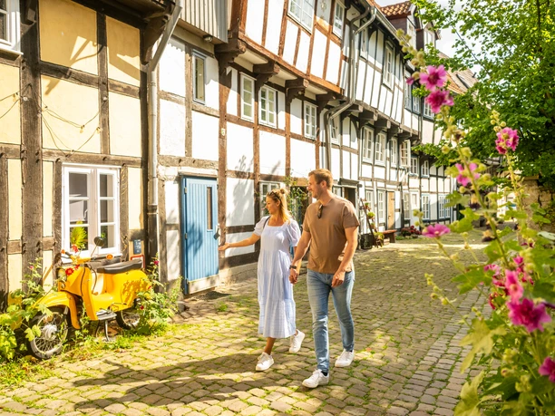 Detmold-2023-211-Adolfstraße-Teutoburger-Wald-Tourismus-D-Ketz.jpg Ein Paar spaziert bei Sonnenschein durch eine idyllische Fachwerkgasse in Detmold.