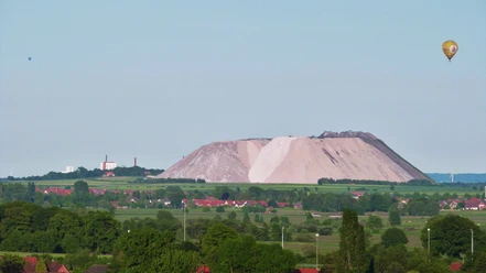 Kalimanscharo Große Halde aus Salzabraum in grüner Landschaft mit einem Heißluftballon am klaren Himmel im Hintergrund.