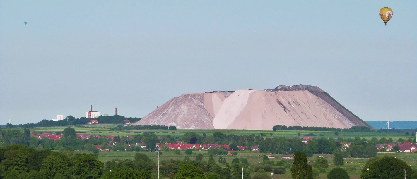 Kalimanscharo Große Halde aus Salzabraum in grüner Landschaft mit einem Heißluftballon am klaren Himmel im Hintergrund.